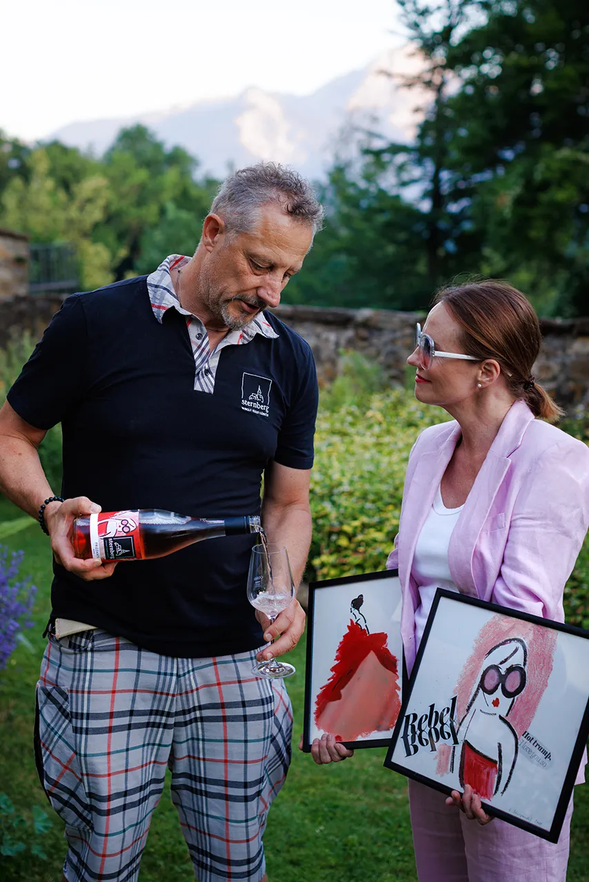 Künstlerin Romy Schwingenschuh präsentiert die Banderole für den Frizzante Rosé 2025. Am Bild v.l.n.r. Winzer Alexander Egger, Romy Schwingenschuh